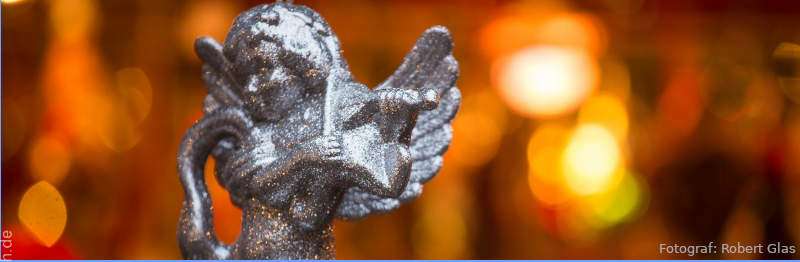 Ein silberner Engel hängt auf einem Weihnachtsmarkt vor unscharfem, orange-roten Hintergrund